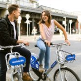 A man and woman laughing while riding bicycles on a city street.