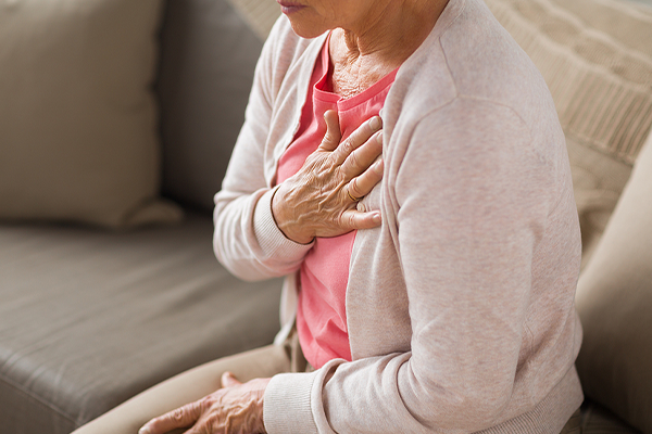 Older woman sitting on sofa with hand over heart.