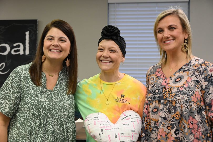 A breast cancer survivor holding a heart-shaped pillow poses for a photo with two women who were part of her treatment team.