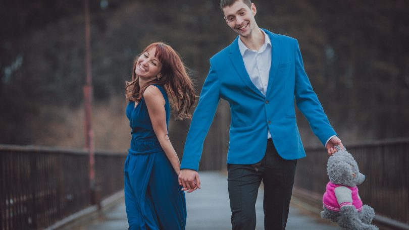 A man wearing a blue sport coat is hoding the hand of a woman wearing a blue dress. Blue is the color of the ribbon signaling Prostate Cancer Awareness Month.