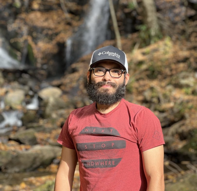 Luis Valente, a sarcoma survivor, wearing a ballcap, eyeglasses, and a red T-shirt while enjoying sunshine outdoors.