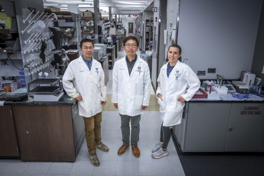 In this photo, you see two men and a woman standing and posing for a photo inside a science lab.
