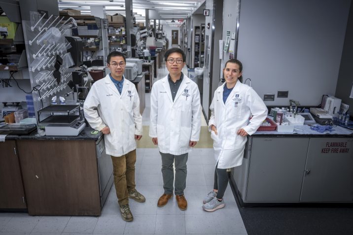 In this photo, you see two men and a woman standing and posing for a photo inside a science lab.