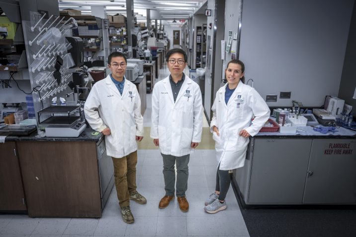 In this photo, you see two men and a woman standing and posing for a photo inside a science lab.