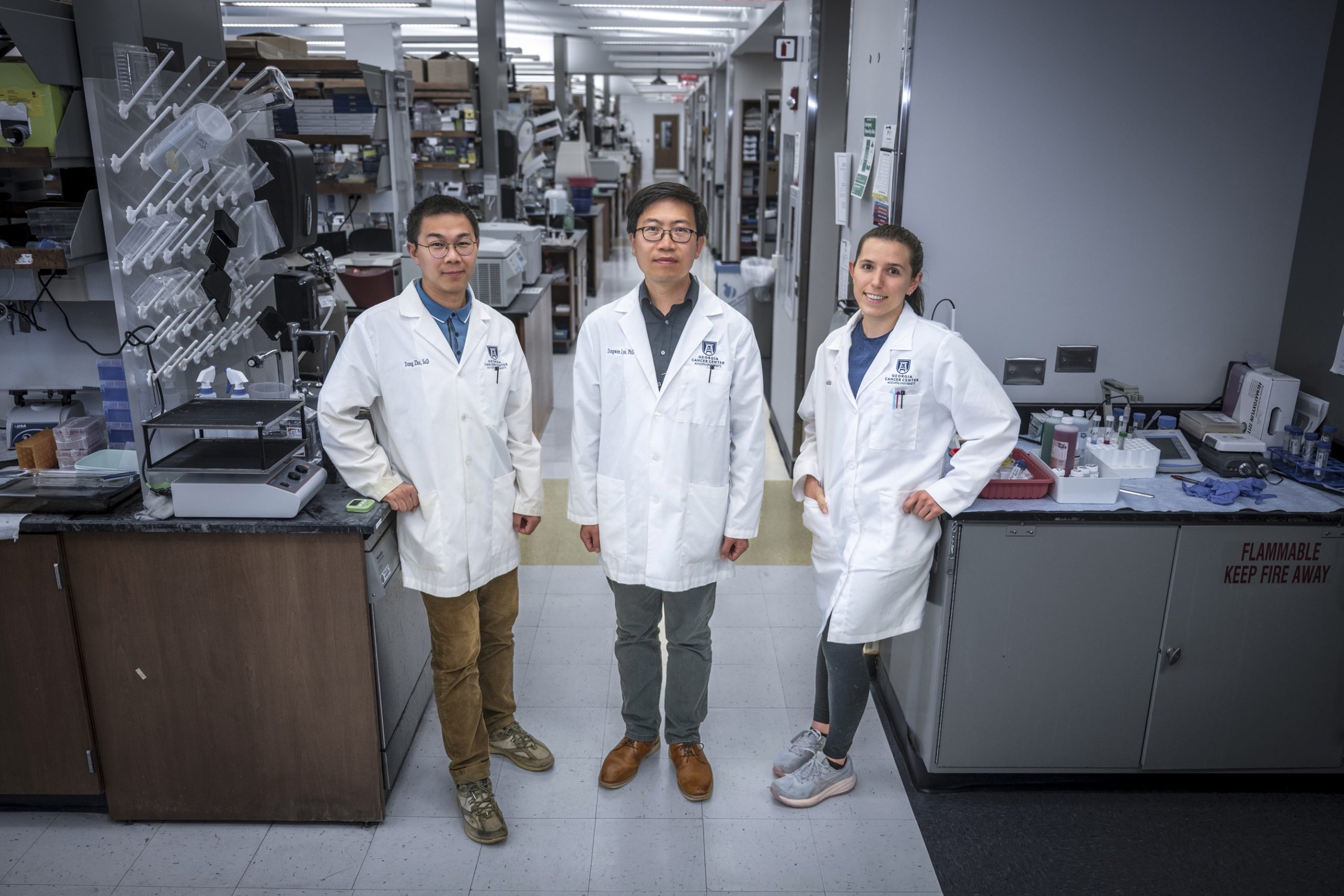 In this photo, you see two men and a woman standing and posing for a photo inside a science lab.