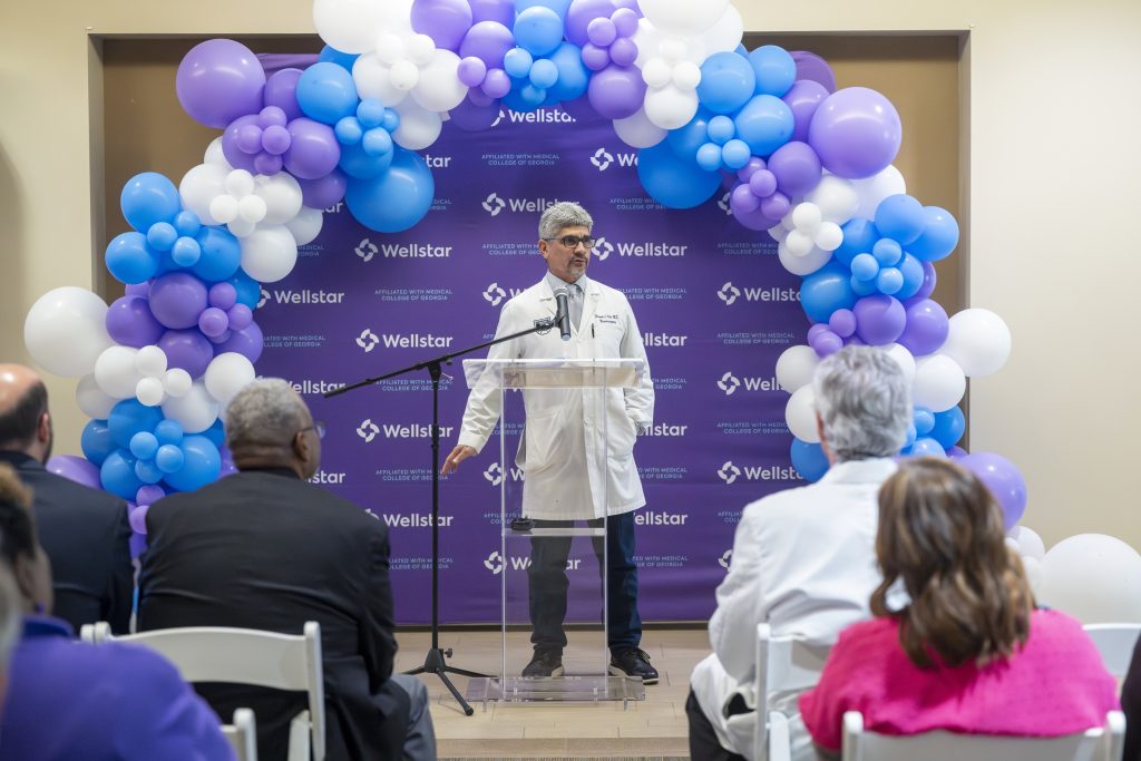 In this photo, you see Dr. Fernando Vale, a man, standing in front of a microphone and lectern giving a speech during a Ribbon Cutting Ceremony.
